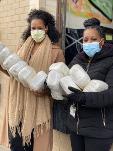 Photo of two Black women dressed warmly posing for the camera and carrying packs of diapers