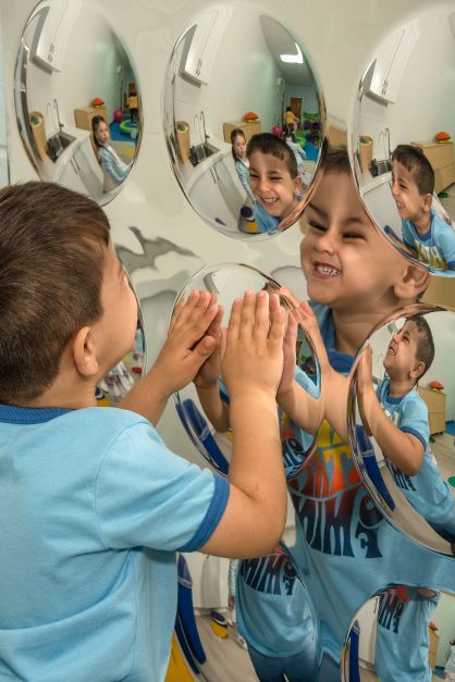 Photo of a young child making a face at a wall of circular mirrors