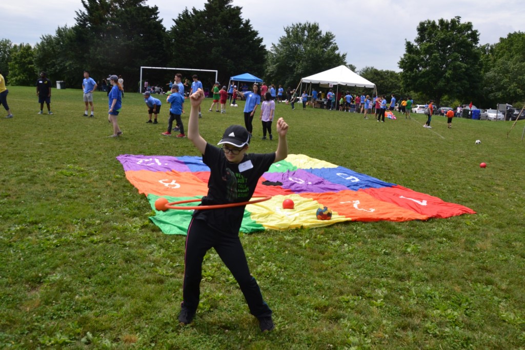 A person wearing all black and a cap playing with a hula hoop at an outdoor sports festival