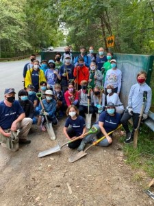 Group photo taken by a forested area with everyone wearing face masks and some holding shovels in hand
