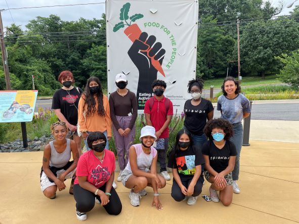Group of summer youth staff posing with masks on outside the Food Justice exhibit at the Smithsonian Anacostia Community Museum