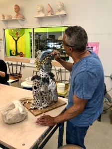 A man wearing glasses and a striped blue shirt working on his ceramic sculpture during a VisArts workshop.