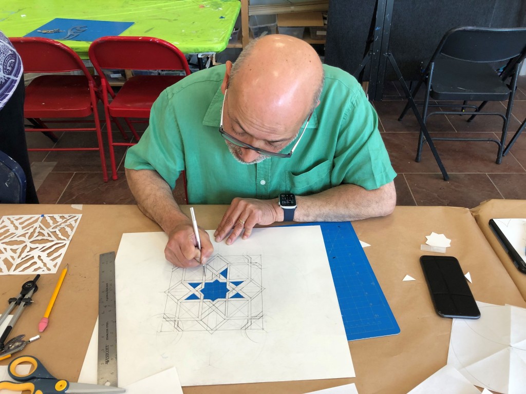 A man wearing glasses and a green polo shirt is cutting out a complex geometric paper design in one of VisArts' paper-cutting workshops.
